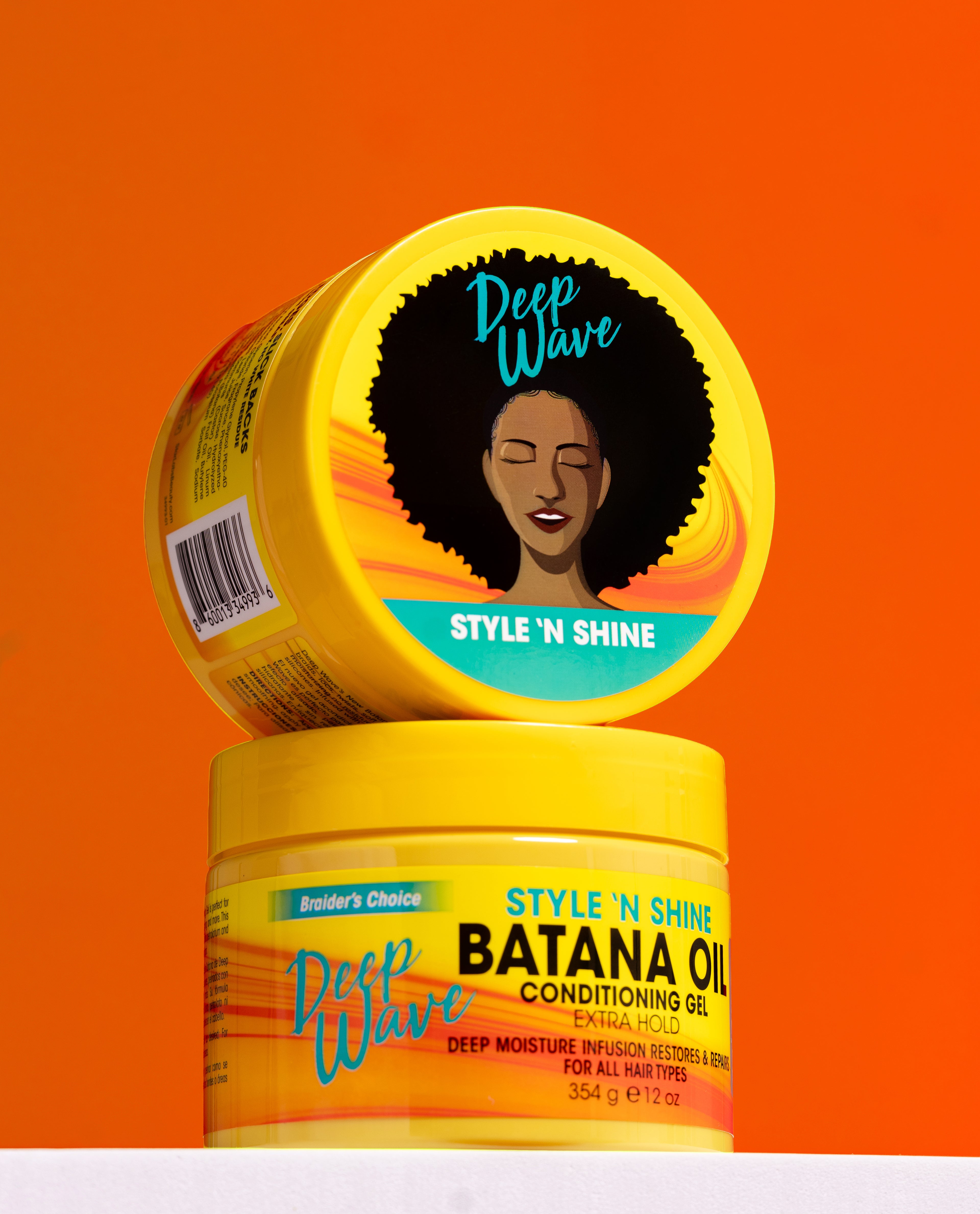 Two yellow haircare containers from Deep Wave Braider's Choice stacked on a white surface against a bright orange background. The top container shows the lid with an illustration of an afro and the text 'Style 'N Shine', while the bottom container reads 'Style 'N Shine Batana Oil Conditioning Oil'.