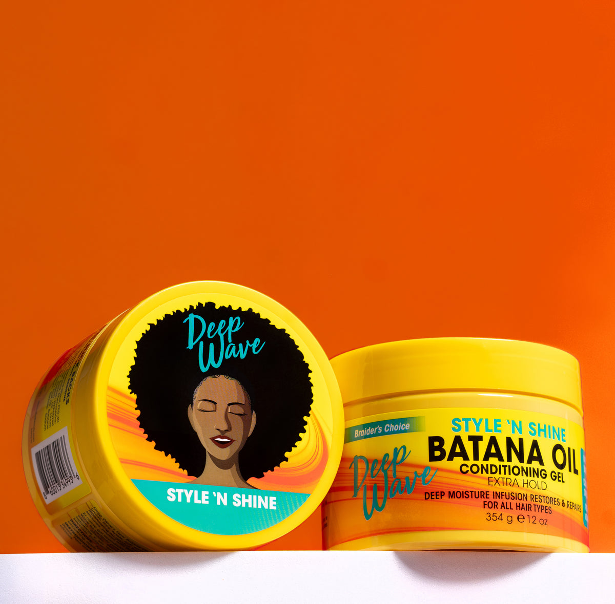 Two yellow Deep Wave hair care product tubs on a white surface against a bright orange background. The tub in front is open, showing the lid label with a Black woman's afro and the text 'Deep Wave Style 'N Shine'.