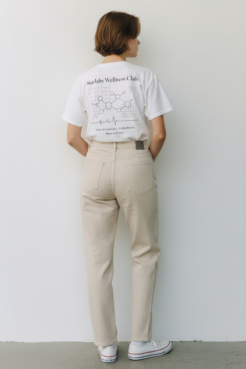 Person wearing a white t-shirt with Starlabs Beauty Wellness Club text and graphics, beige pants, and white sneakers against a plain background