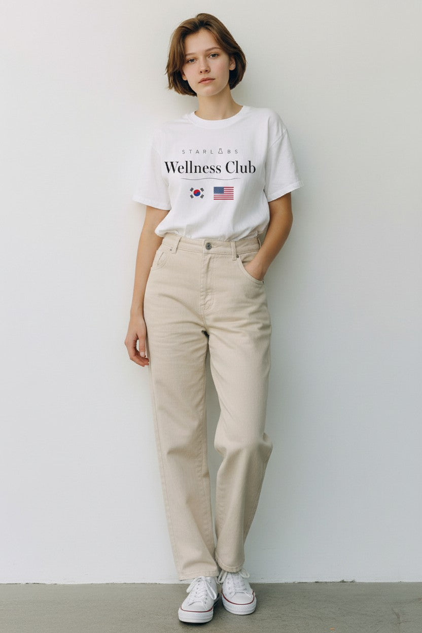 Person wearing a white t-shirt with Starlabs Wellness Club text and beige pants against a plain background